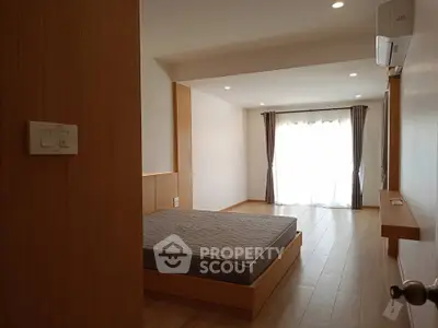 Spacious bedroom with wooden flooring and natural light through large window.