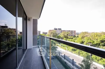 Modern balcony with glass railing offering a stunning view of lush greenery and urban landscape.
