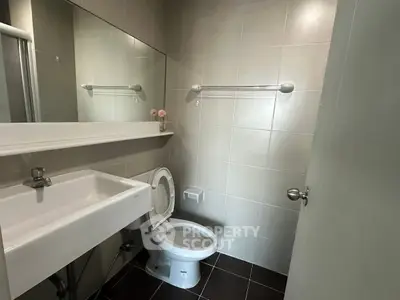 Modern bathroom with sleek fixtures and neutral tiles, featuring a large mirror and a compact sink.