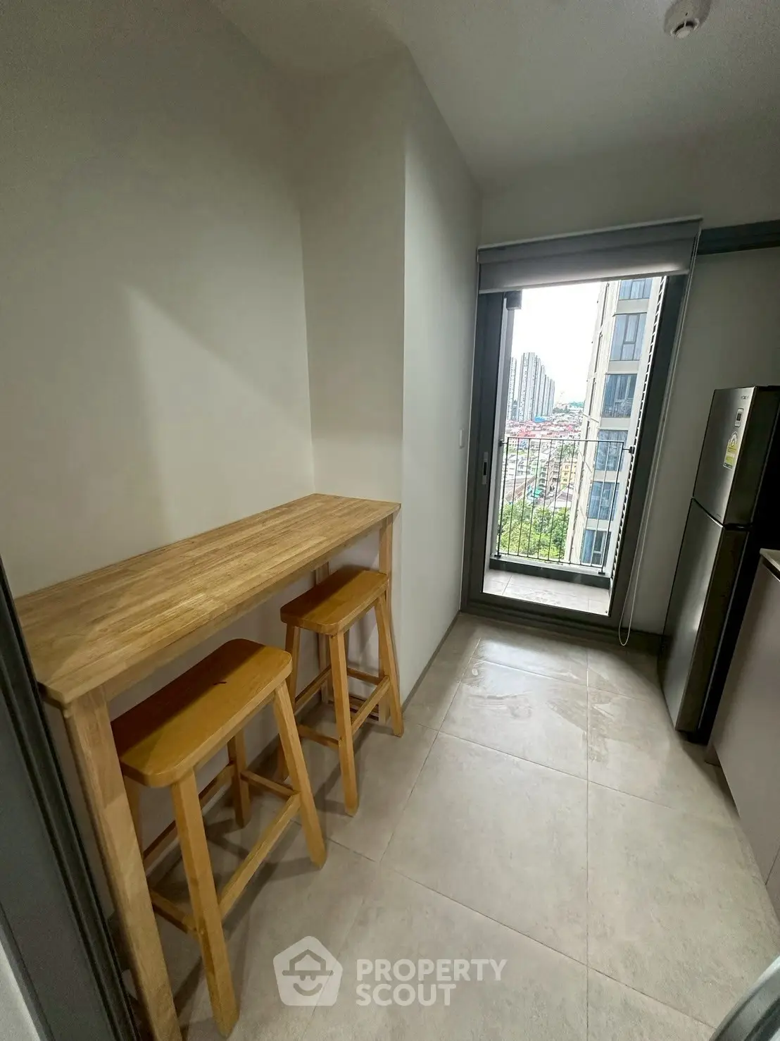 Modern kitchen with tall wooden table and stools, offering a city view through large window.