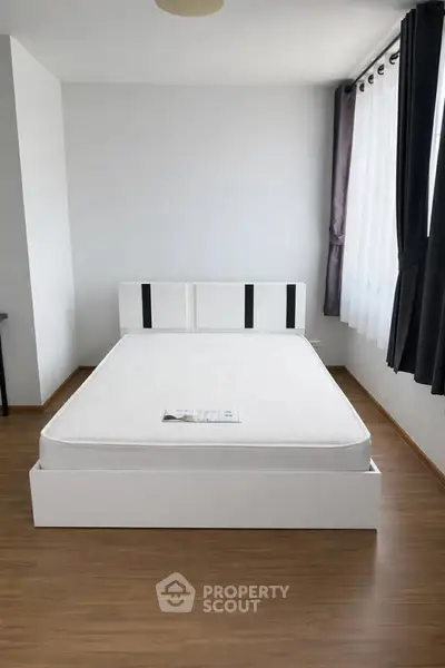 Modern minimalist bedroom with wooden flooring and large window for natural light.