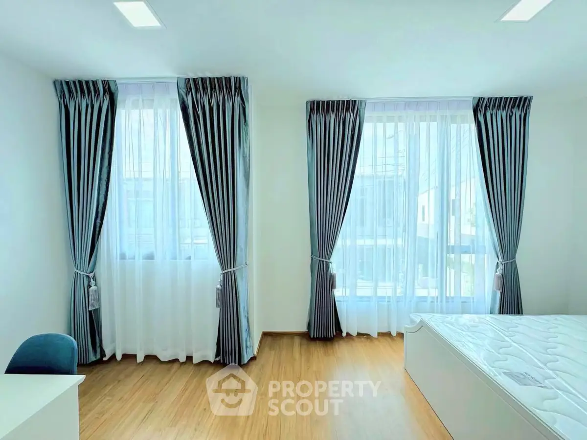 Bright bedroom with large windows and elegant curtains, showcasing modern minimalist design.