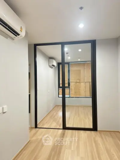 Modern apartment interior with wooden flooring and glass partition, featuring air conditioning.