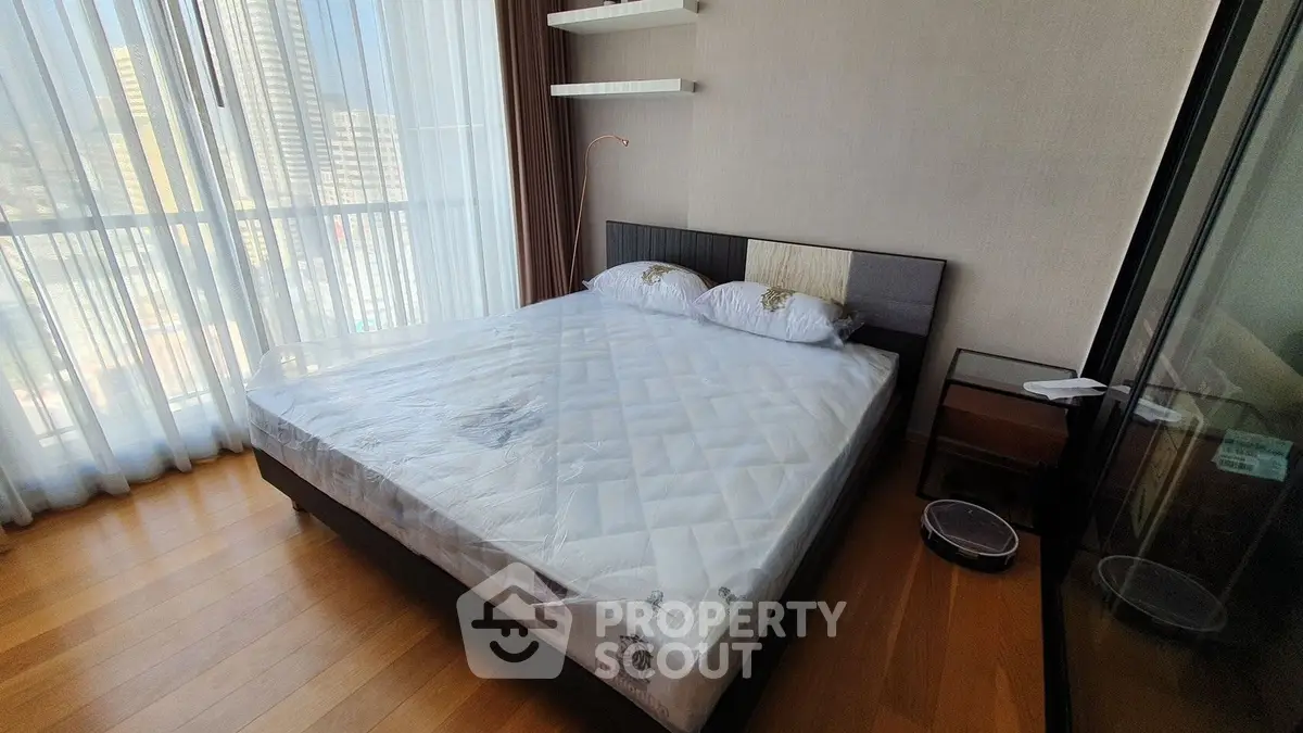 Modern bedroom with large window and hardwood floors in a high-rise apartment.