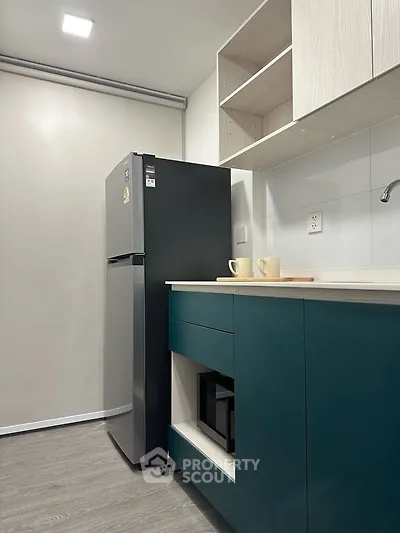 Modern kitchen with sleek fridge and teal cabinetry, perfect for urban living.