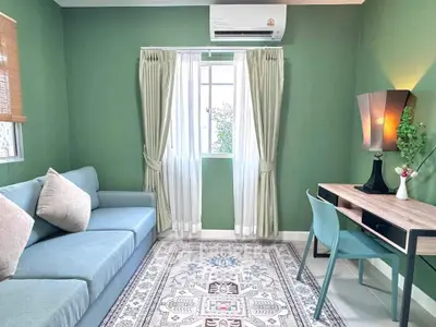 Charming living room with green walls, cozy sofa, and stylish desk, perfect for relaxation and work.