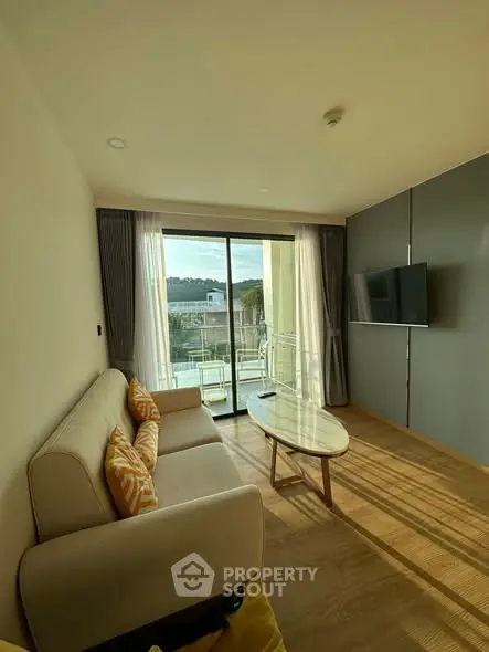 Modern living room with large windows and balcony view, featuring a cozy sofa and wall-mounted TV.