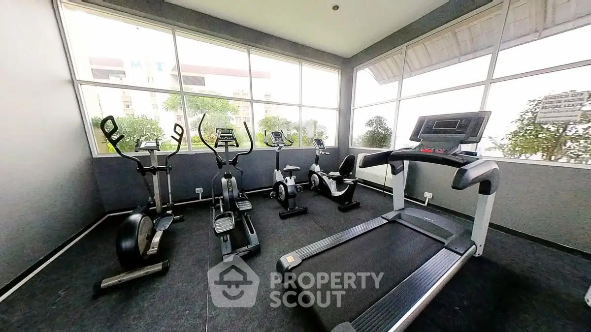 Modern gym with cardio equipment and large windows in a residential building.