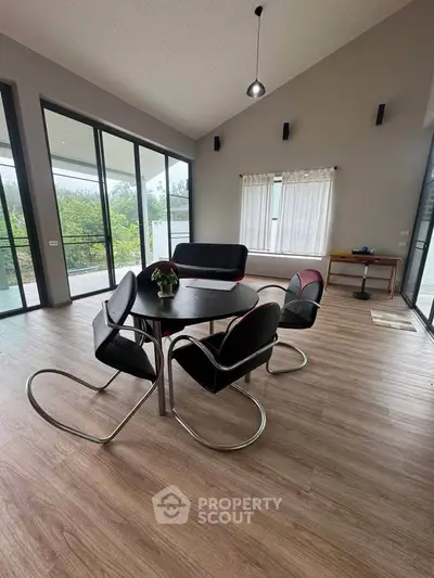 Spacious modern living room with large windows and stylish furniture, offering a serene view of greenery.