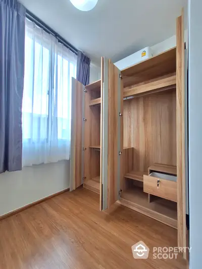 Bright and airy bedroom with spacious wooden wardrobe, laminate flooring, and elegant drapery, perfect for modern living.