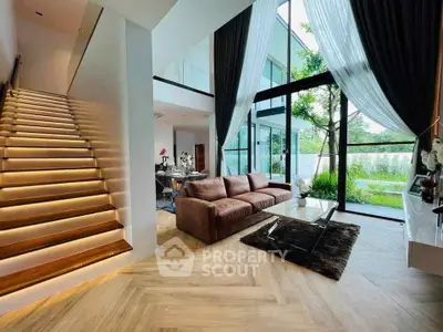 Luxurious modern living room with high ceilings, large windows, and elegant staircase in a contemporary home.