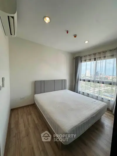 Bright bedroom with large window and city view, featuring a comfortable bed and modern decor.