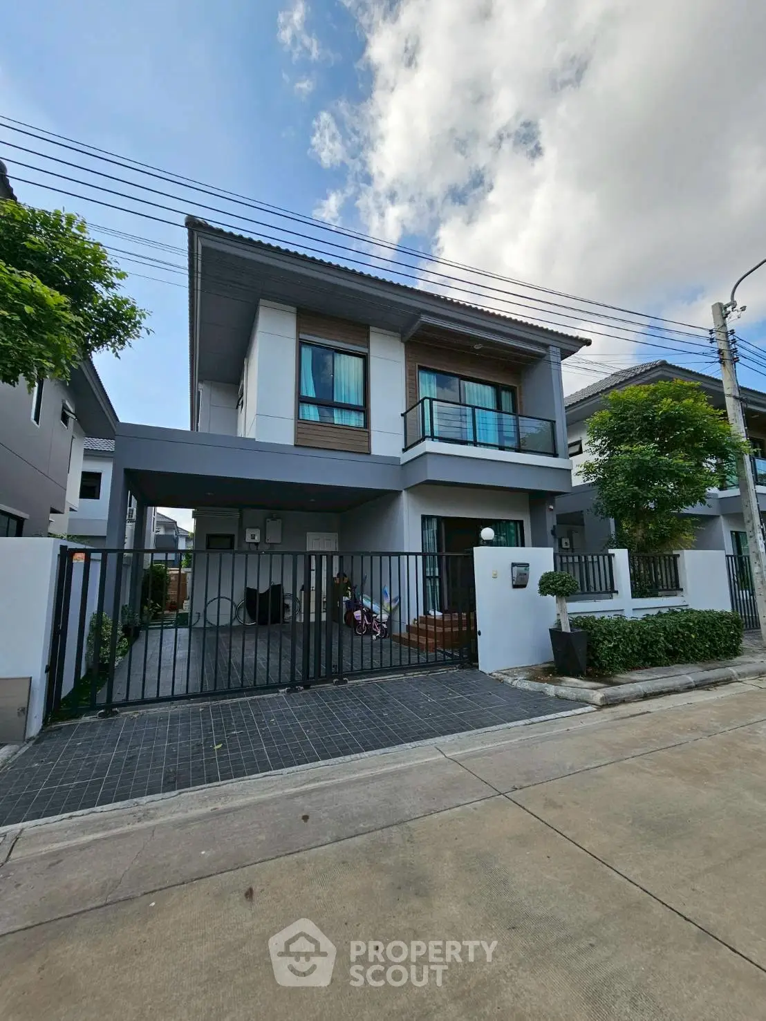 Modern two-story house with balcony and gated driveway in suburban neighborhood