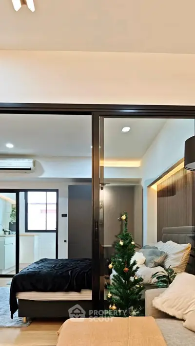 Modern living room with cozy decor and small Christmas tree, featuring a view into a stylish bedroom.