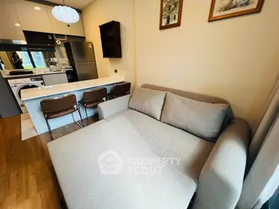 Modern living room with cozy sofa and sleek kitchen featuring stainless steel appliances.