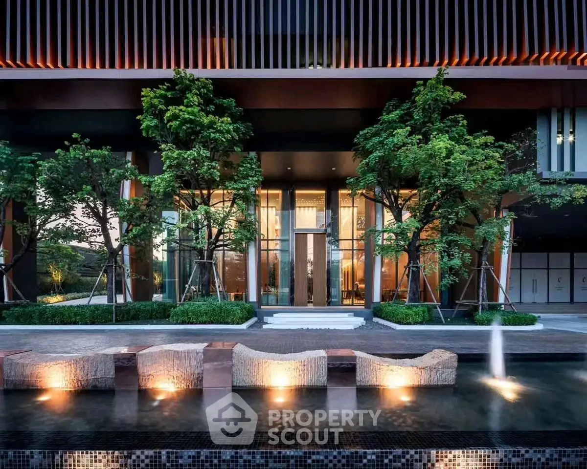 Luxurious modern building entrance with elegant water feature and lush greenery.