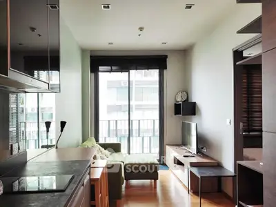 Modern living room with open kitchen, featuring sleek furniture and a large window for natural light.
