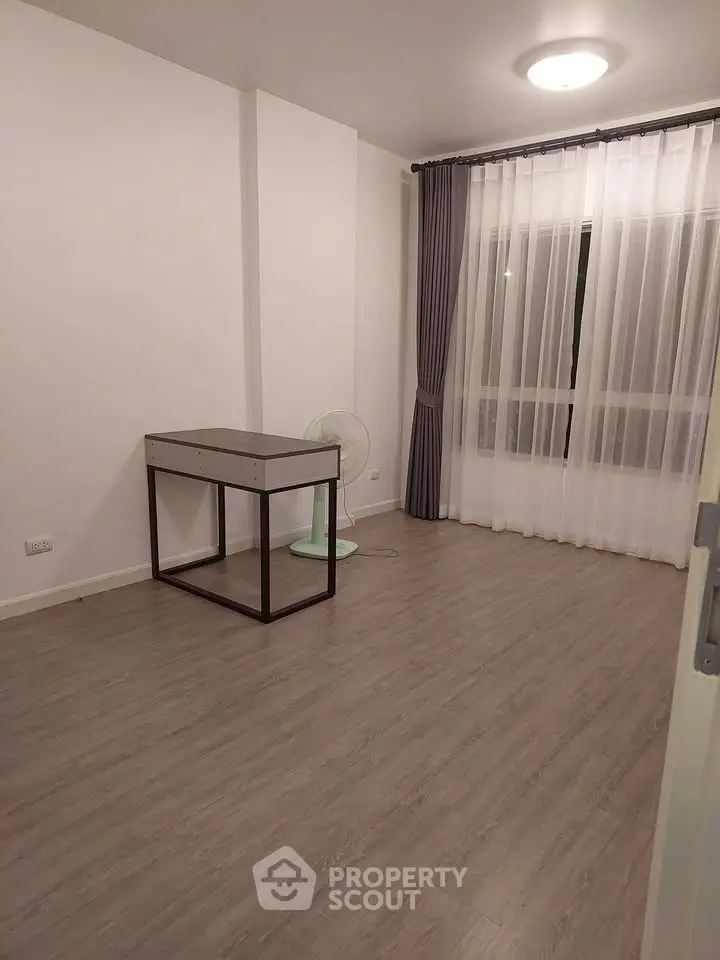 Spacious empty room with modern flooring and large window, ideal for customization.