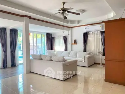 Spacious living room with modern sofas and ceiling fan, featuring large windows and pool view.