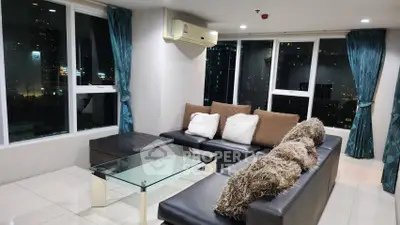 Modern living room with city view, featuring sleek black sofa and glass coffee table.