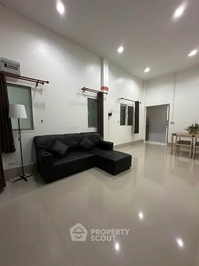 Spacious modern living room with sleek black sofa and elegant dining area, perfect for contemporary living.