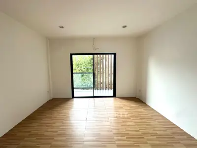 Spacious empty room with wooden flooring and large window overlooking greenery, perfect for customization.