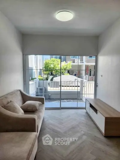 Bright living room with modern sofa and large window overlooking outdoor area.