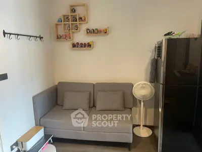 Cozy living room with modern gray sofa, decorative shelves, and sleek black refrigerator.