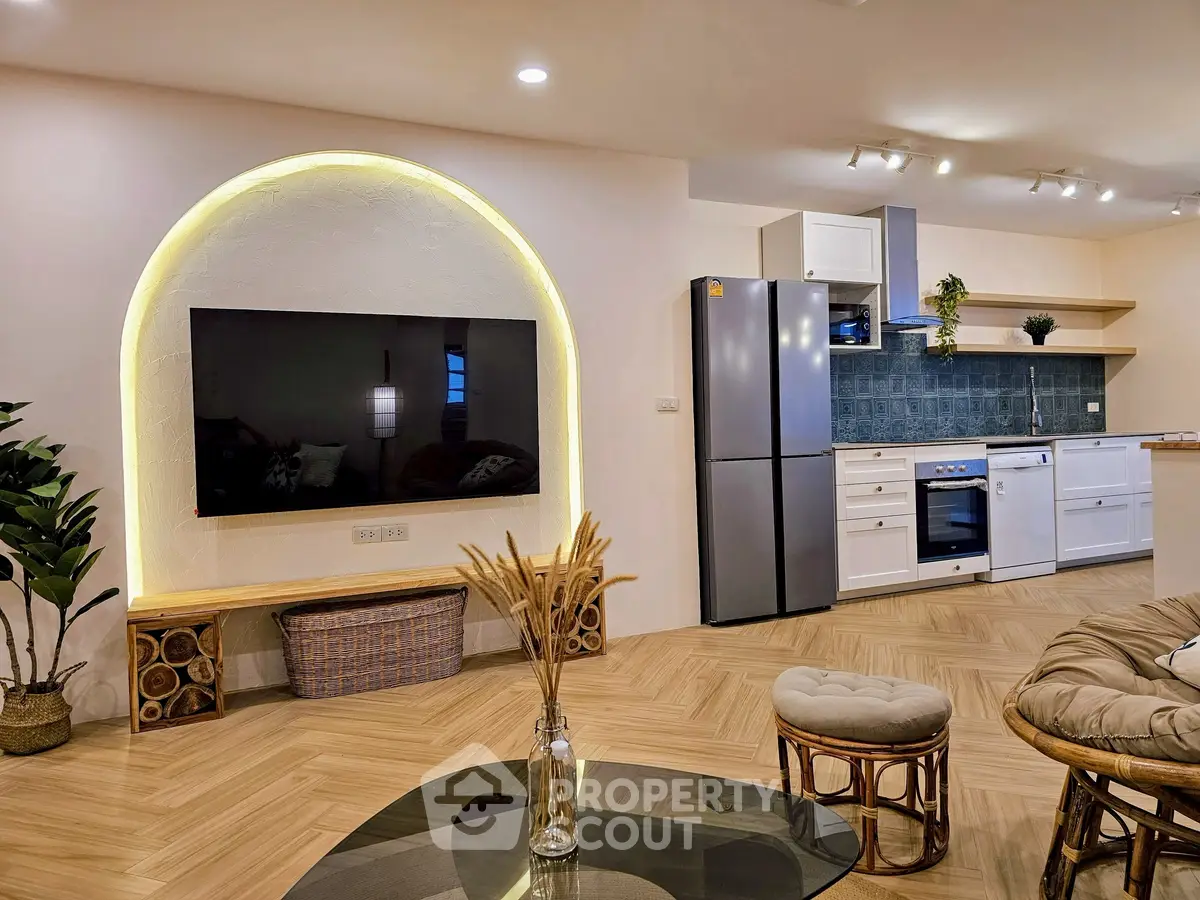 Modern living room with stylish kitchen, featuring large TV and elegant decor.