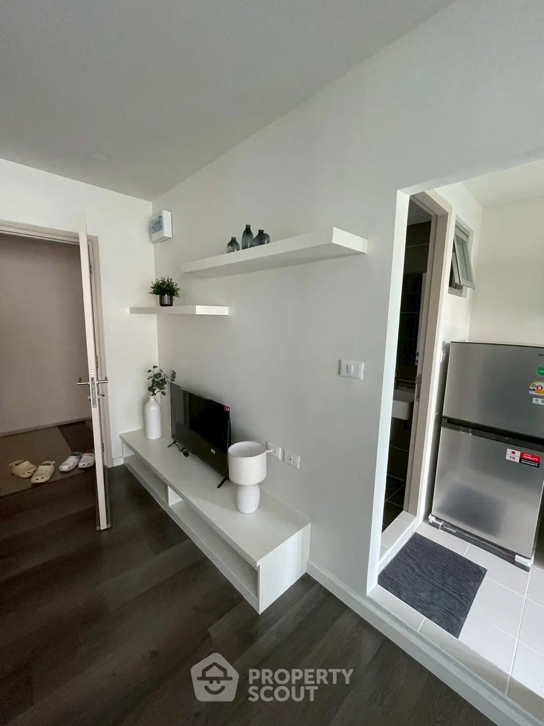 Modern living room with sleek white shelves and compact kitchen area featuring stainless steel fridge.