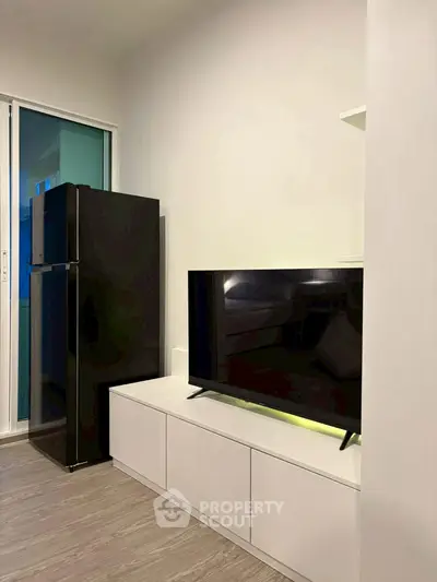 Modern living room with sleek TV and refrigerator, showcasing minimalist design and functionality.