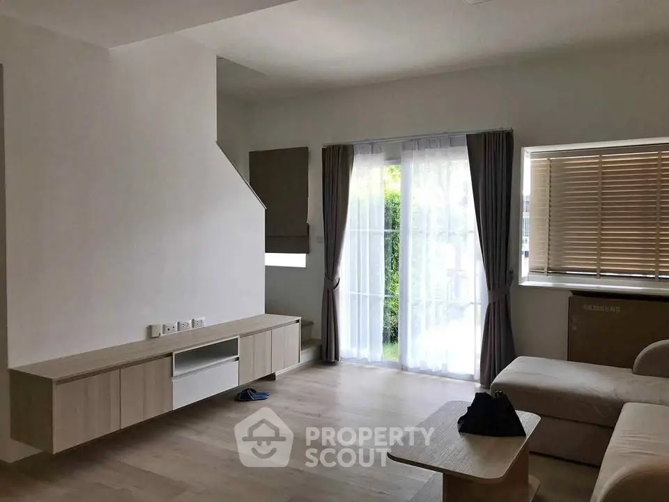 Spacious modern living room with natural light and minimalist decor, featuring large windows and elegant curtains.