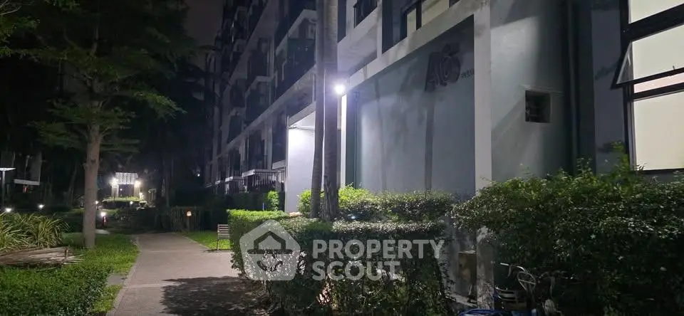 Night view of modern apartment building with well-lit pathway and lush greenery.