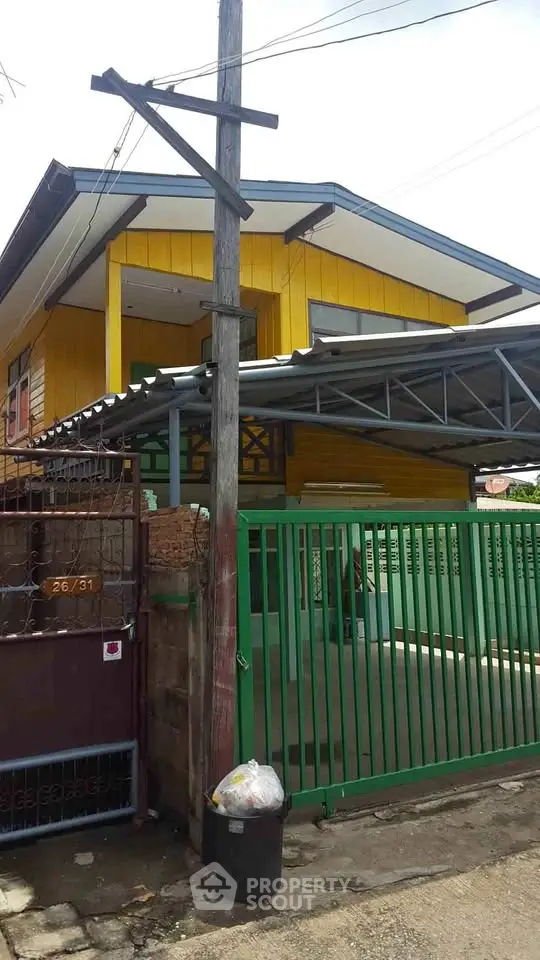 Charming yellow house with green gate and covered carport in a residential neighborhood.