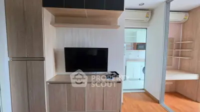 Modern living room with built-in wooden cabinets and TV, adjacent to a kitchen area.