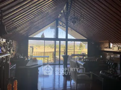 Charming attic living room with rustic decor and stunning countryside view from large windows.