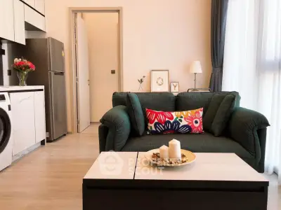 Modern living room with stylish sofa and open kitchen layout, featuring sleek appliances and elegant decor.