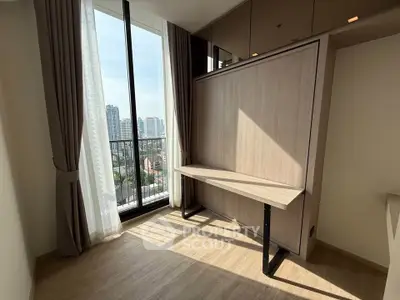 Modern room with large window and city view, featuring a sleek wooden desk and light wood flooring.