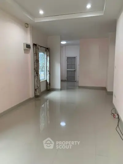 Spacious empty room with glossy tiled floor and large window, ideal for customization.