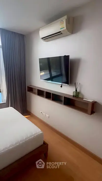 Modern bedroom with wall-mounted TV and air conditioning, featuring sleek wooden flooring and minimalist decor.