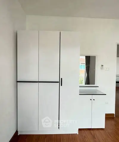 Modern minimalist bedroom with sleek white wardrobe and wooden flooring.