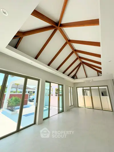 Spacious modern living room with high wooden beam ceiling and large glass doors opening to a bright patio.