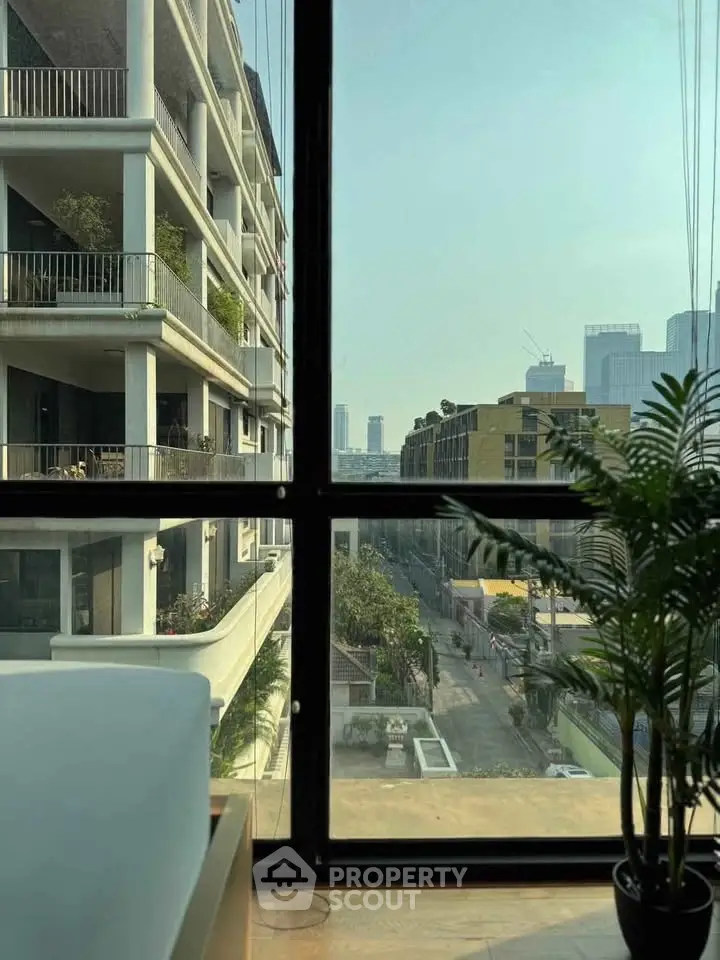 Stunning urban view from a modern apartment window with lush greenery and city skyline.