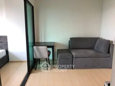 Modern living room with sleek gray sofa and compact dining area in stylish apartment.