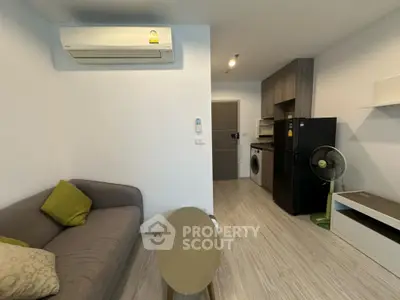 Modern living room with air conditioning, sofa, and compact kitchen featuring washing machine and fridge.