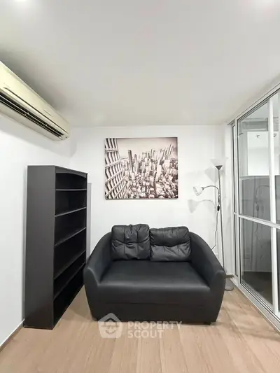 Modern living room with black sofa, bookshelf, and cityscape artwork, featuring sleek design and natural light.