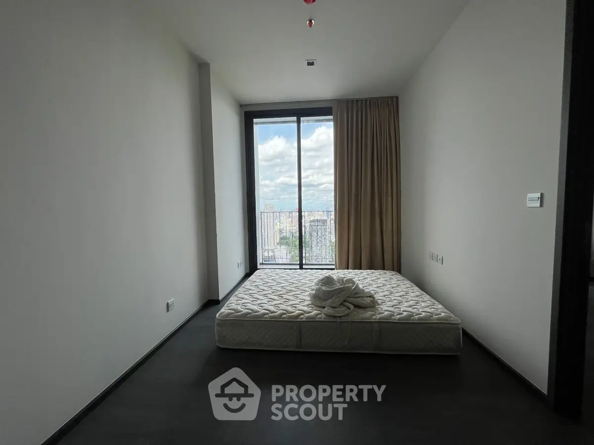 Minimalist bedroom with large window offering stunning city view, featuring a simple mattress and elegant dark flooring.