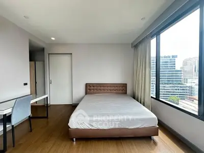 Spacious bedroom with large window offering city views, featuring a comfortable bed and a study desk.