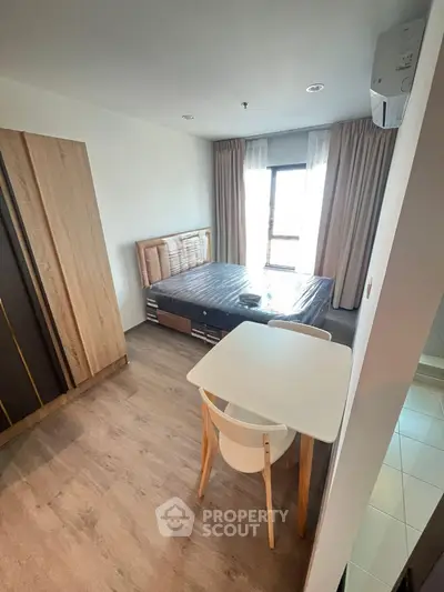 Modern bedroom with wooden flooring, stylish bed, and cozy dining area near window.