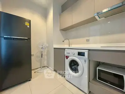 Modern kitchen with sleek appliances including fridge, washing machine, and microwave in a compact layout.